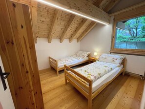 Une chambre avec deux lits en bois, une fenêtre donnant sur un paysage verdoyant et un plafond en pente.