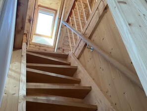 Un escalier en bois avec une rampe métallique, menant à une lucarne.