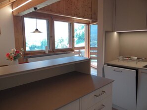 A kitchen with a wooden ceiling, a window with a view of trees, and a countertop with a vase of flowers.