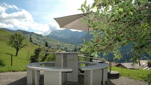 A circular stone table with a bench, surrounded by a large umbrella, set against a scenic mountain backdrop. - Serene Farmhouse in Habkern with Parking (Habkern)