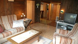 A cozy living room with a sofa, armchair, and a coffee table. There is a television on a stand and a lamp on a side table. - Serene Farmhouse in Habkern with Parking (Habkern)