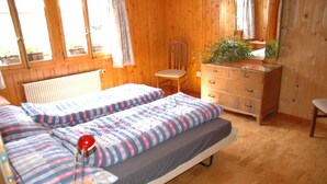 A room with wooden walls, a bed with striped bedding, a dresser, a chair, and a radiator. - Serene Farmhouse in Habkern with Parking (Habkern)