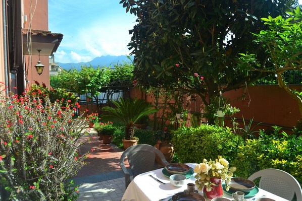 An outdoor dining area with a table set for two, surrounded by potted plants and a view of mountains.