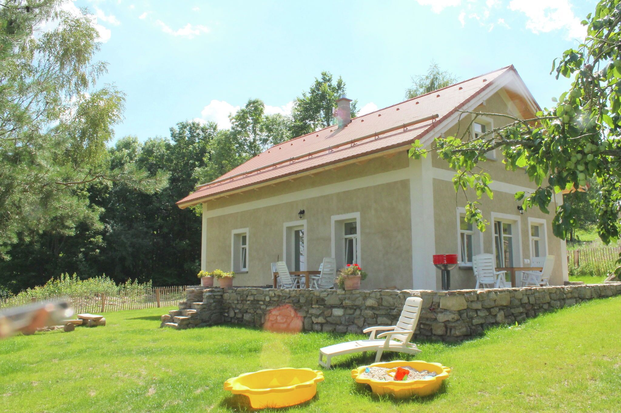 Ein Haus mit steinernem Fundament, rotem Dach und einer Veranda mit Gartenmöbeln.