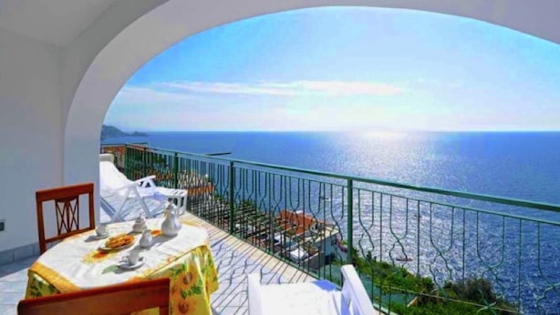 A dining area with a table set for two, overlooking a coastal view. - Belvilla by OYO Oasi Blu (Praiano)