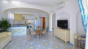 A spacious living area with a kitchen, dining table, and a TV. - Belvilla by OYO Oasi Blu (Praiano)