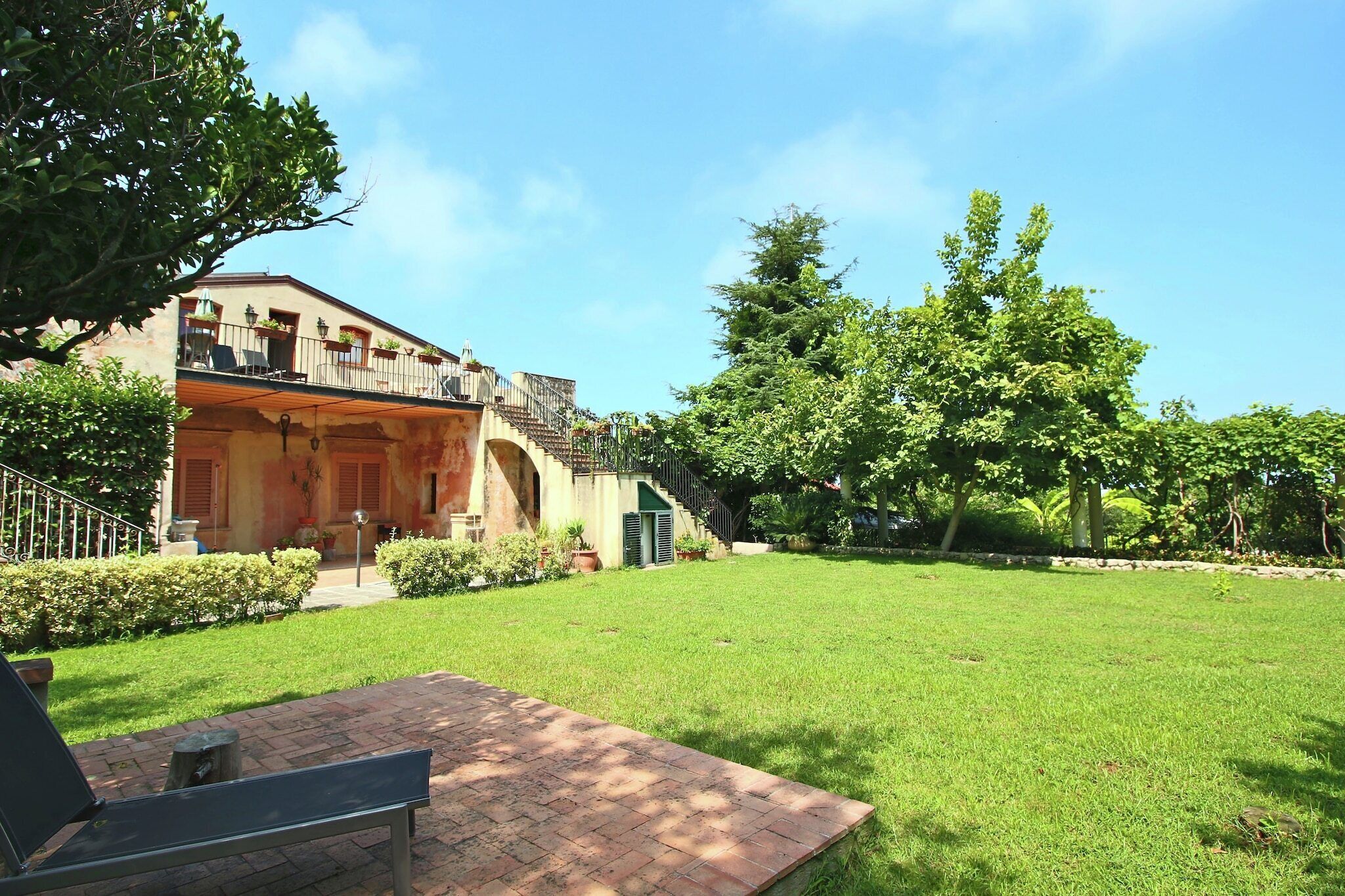 A building with a balcony, a grassy yard, and a paved area with a bench.