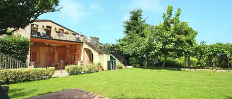 A building with a balcony, a grassy yard, and a paved area with a bench.