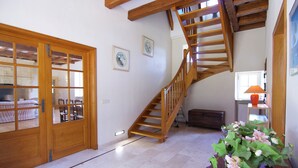 A spacious room with a wooden staircase, a large wooden door, and a small table with a flower arrangement.