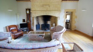 A living room with a stone fireplace, leather armchairs, a television, and a clock.