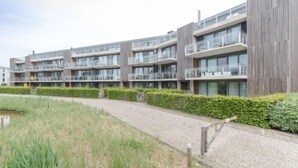 A modern multi-story residential building with balconies, a paved walkway, and a small pond.
