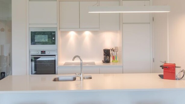 A modern kitchen with a central island, a built-in oven, a coffee maker, and a red appliance on the counter.