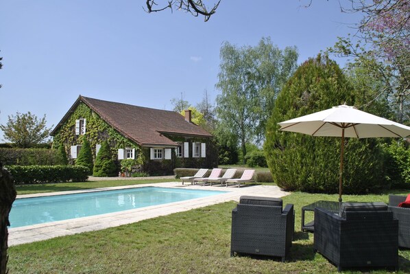 A house with a swimming pool, surrounded by a well-maintained lawn and trees.