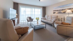 Un salon moderne avec un téléviseur à écran plat, un canapé, un fauteuil et une table basse.