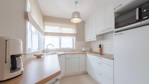 Une cuisine moderne avec des meubles blancs, un plan de travail en bois, un four encastré et un réfrigérateur en acier inoxydable.