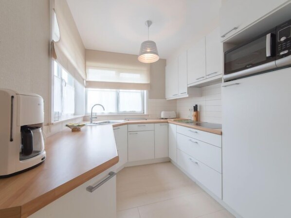 A modern kitchen with white cabinetry, a wooden countertop, a built-in oven, and a stainless steel refrigerator.