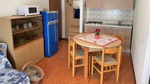 Uma cozinha compacta com micro-ondas, geladeira azul e fogão. Há uma mesa de jantar com cadeiras e um tapete pequeno.