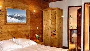 A wooden room with a bed, a wooden wardrobe, a framed picture of a mountain, and a small table with a vase. - Luxury flat with sauna in the French Alps (Champagny en Vanoise)