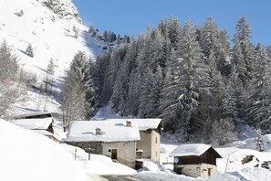 A snow-covered village with traditional buildings, a clear sky, and a forested mountain backdrop.