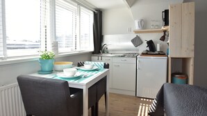 A compact kitchen with white cabinets, a small refrigerator, and a window with blinds. - Elegant studio near beach (Bergen aan Zee)