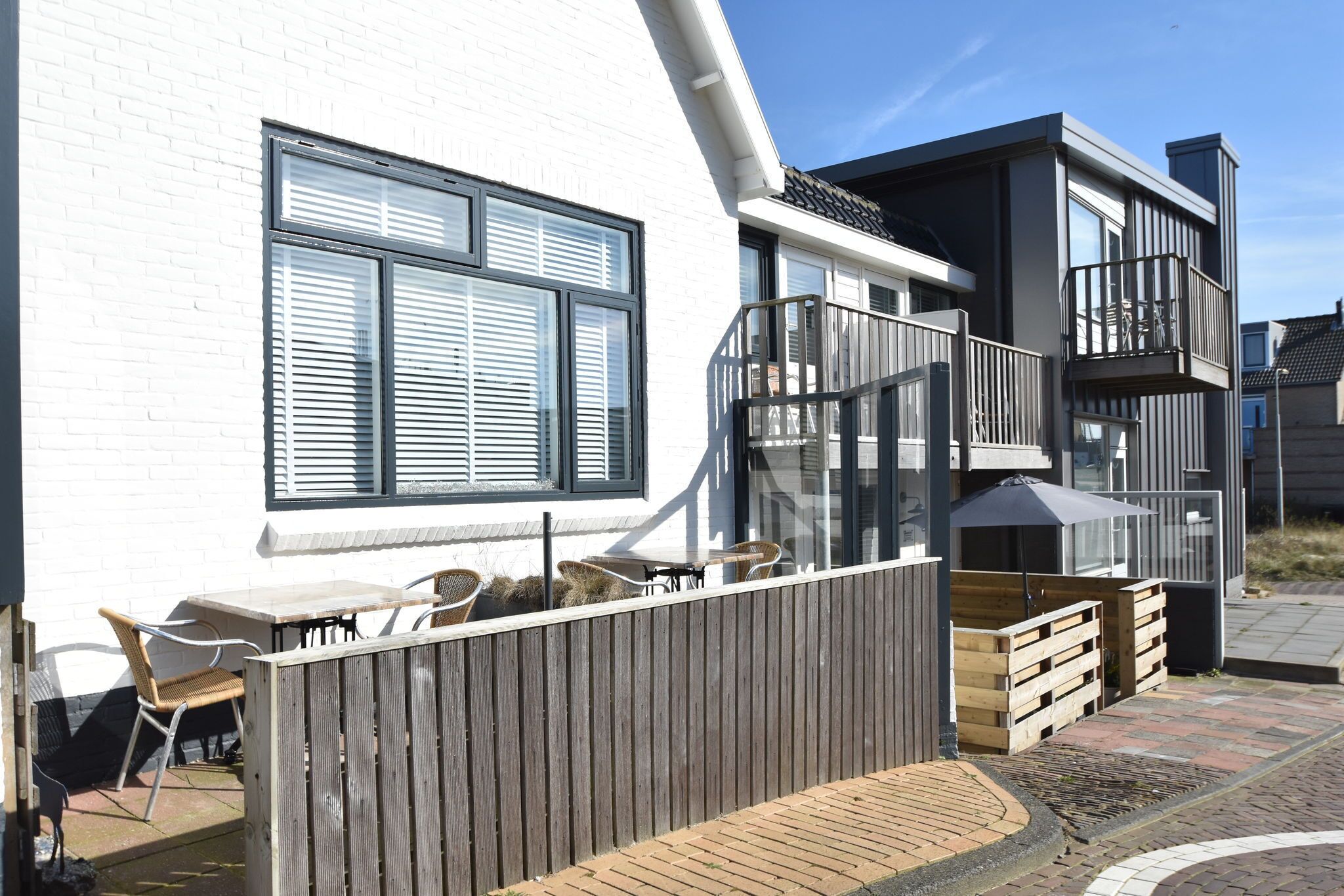 A modern building with a white exterior, large windows, and a balcony with outdoor furniture.