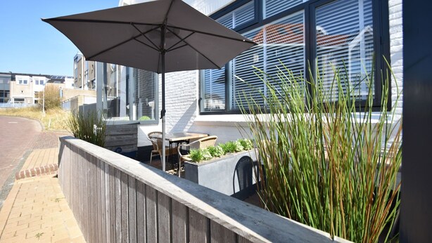 An outdoor patio with a table and chairs, a large umbrella, and a planter with plants. - Elegant studio near beach (Bergen aan Zee)