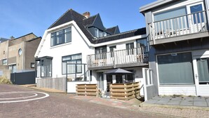 A two-story residential building with a balcony, a covered outdoor seating area, and a garage. - Elegant studio near beach (Bergen aan Zee)