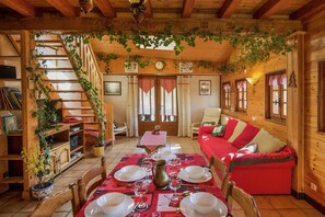 A cozy wooden cabin interior with a dining table set, a staircase with greenery, and a red sofa. - Chalet in Rhone Alpes with Stunning Views (Abondance)