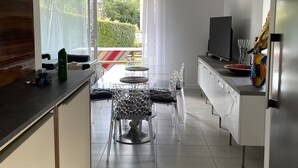 A modern kitchen with a dining area, featuring a large window, a flat-screen TV, and a refrigerator. - House 87 M2 in closed and secured residence 500m from the beach (Capbreton)