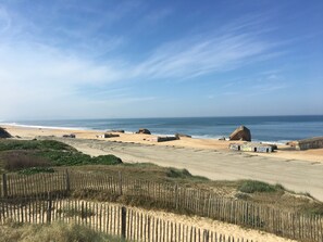 A beach with large rocks, a sandy path, and a wooden fence.