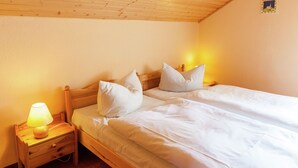 Un lit double avec une literie et des oreillers blancs, une table de chevet en bois avec une lampe et un petit tiroir.