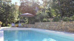 A swimming pool with stone walls and a patio area with chairs and an umbrella. - Modern gîte with pool on large property of owner, 1 km from Provençal village (Faucon)
