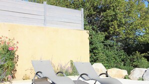 Two sun loungers with metal frames and white cushions, positioned on a gravel surface, with a yellow wall and greenery in the background. - Modern gîte with pool on large property of owner, 1 km from Provençal village (Faucon)