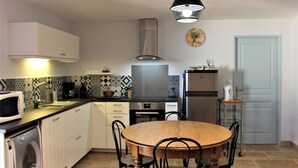A compact kitchen with white cabinets, a microwave, a sink, a stove, and a dining table with chairs. - Modern gîte with pool on large property of owner, 1 km from Provençal village (Faucon)