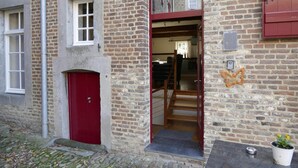 A brick building with a red door, a staircase leading to an upper level, and a small table with a potted plant outside.