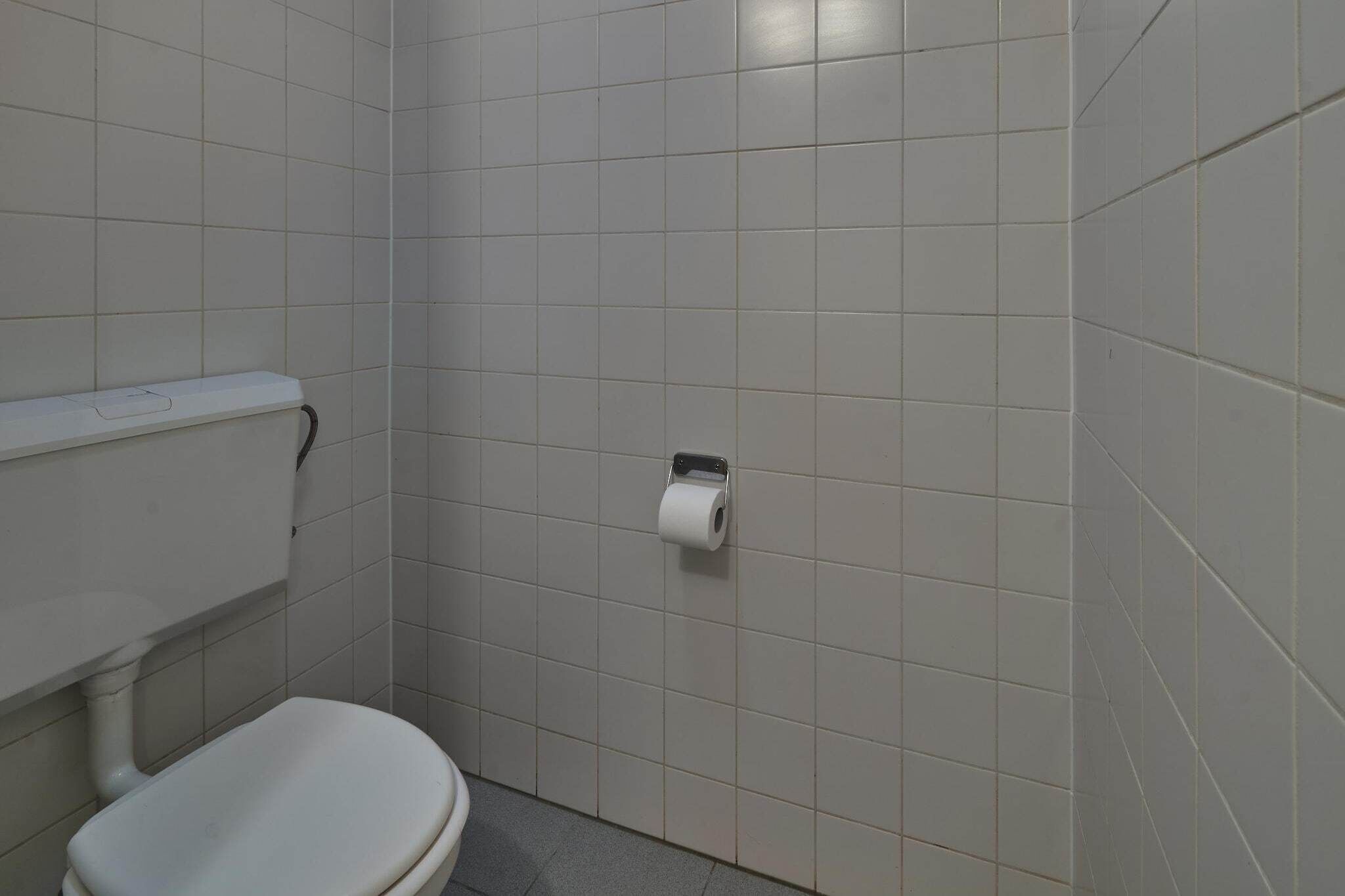 Une petite salle de bain propre, avec des carreaux blancs, des toilettes et un distributeur de serviettes en papier.