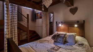 A cozy bedroom with a wooden headboard, a quilted bedspread, and a staircase leading to an upper level.