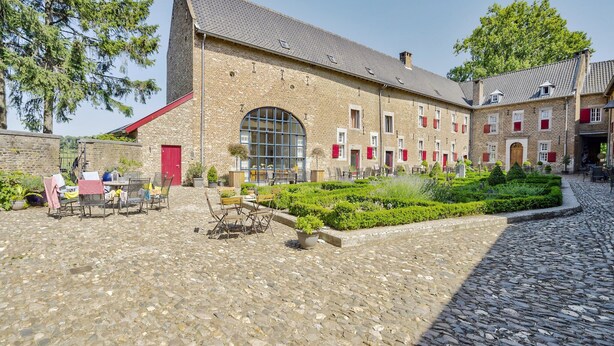 A courtyard with a cobblestone floor, a large building with a red door, and neatly trimmed hedges.