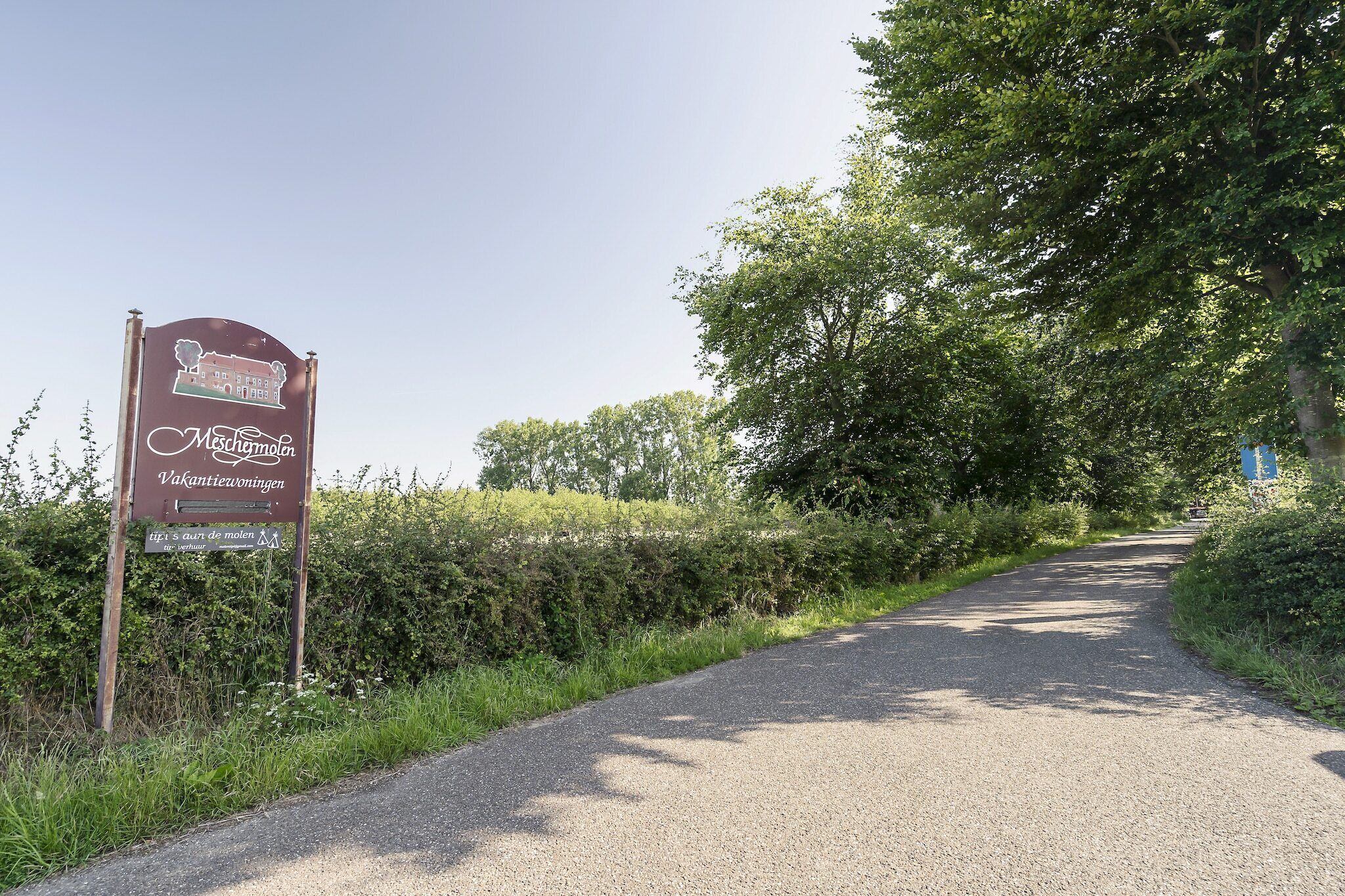 Señal de un hotel llamado 'Meschimowen' que muestra una carretera rural y follaje verde.