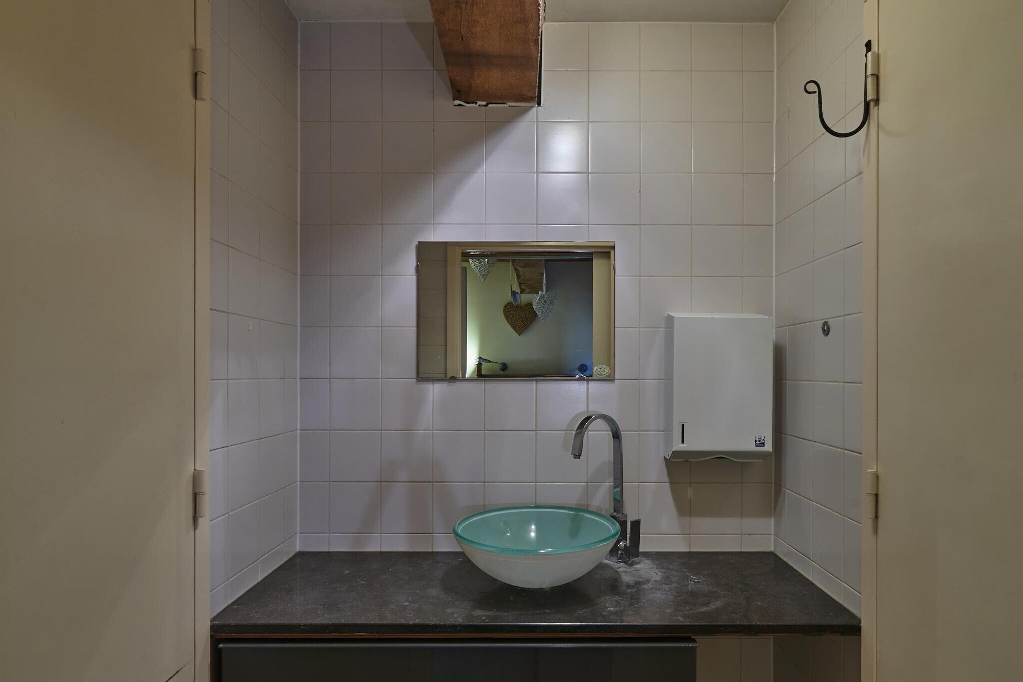 A bathroom with white tiled walls, a glass sink, a mirror, and a towel rack.