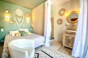 A bedroom with a bed, a chair, a vanity with a mirror, and wall decor.
