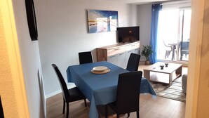 En matplats med ett bord dukat för två personer, en tv-apparat på ett träskåp och ett fönster med blå gardiner.