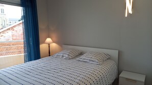 En snyggt bäddad säng med ett täcke med prickmönster, en sänglampa och ett nattduksbord med lådor.