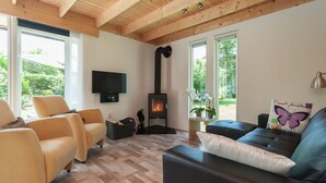 Un salon chaleureux avec une cheminée, des sièges confortables et de grandes fenêtres donnant sur un paysage verdoyant.