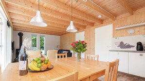 Une table de salle à manger en bois, des chaises, un vase avec des fleurs et un panier de fruits.