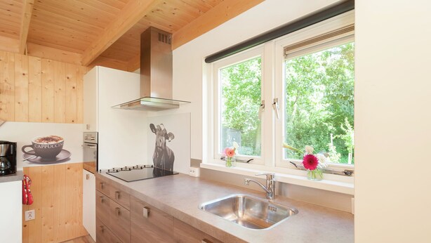 Une cuisine moderne avec des meubles en bois, un évier en acier inoxydable et une fenêtre donnant sur un paysage verdoyant.