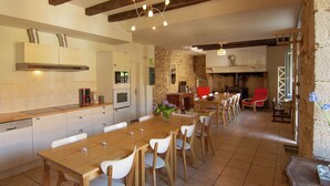A spacious kitchen with a wooden dining table and chairs, a built-in oven, and a stone wall. - Holiday Home in Saint-Léonard with Pool (Saint Léonard de Noblat)