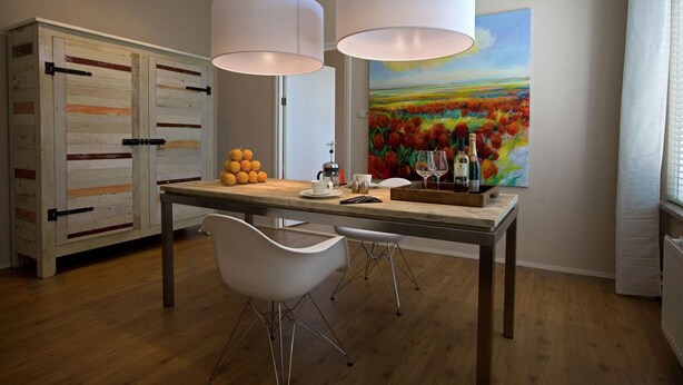 A dining area with a wooden table, white chairs, a painting of a field of flowers, and a cabinet with a rustic design.