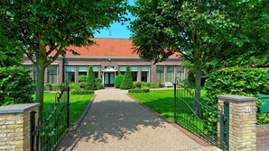 A pathway leading to a building with a red-tiled roof, surrounded by greenery and a metal fence.