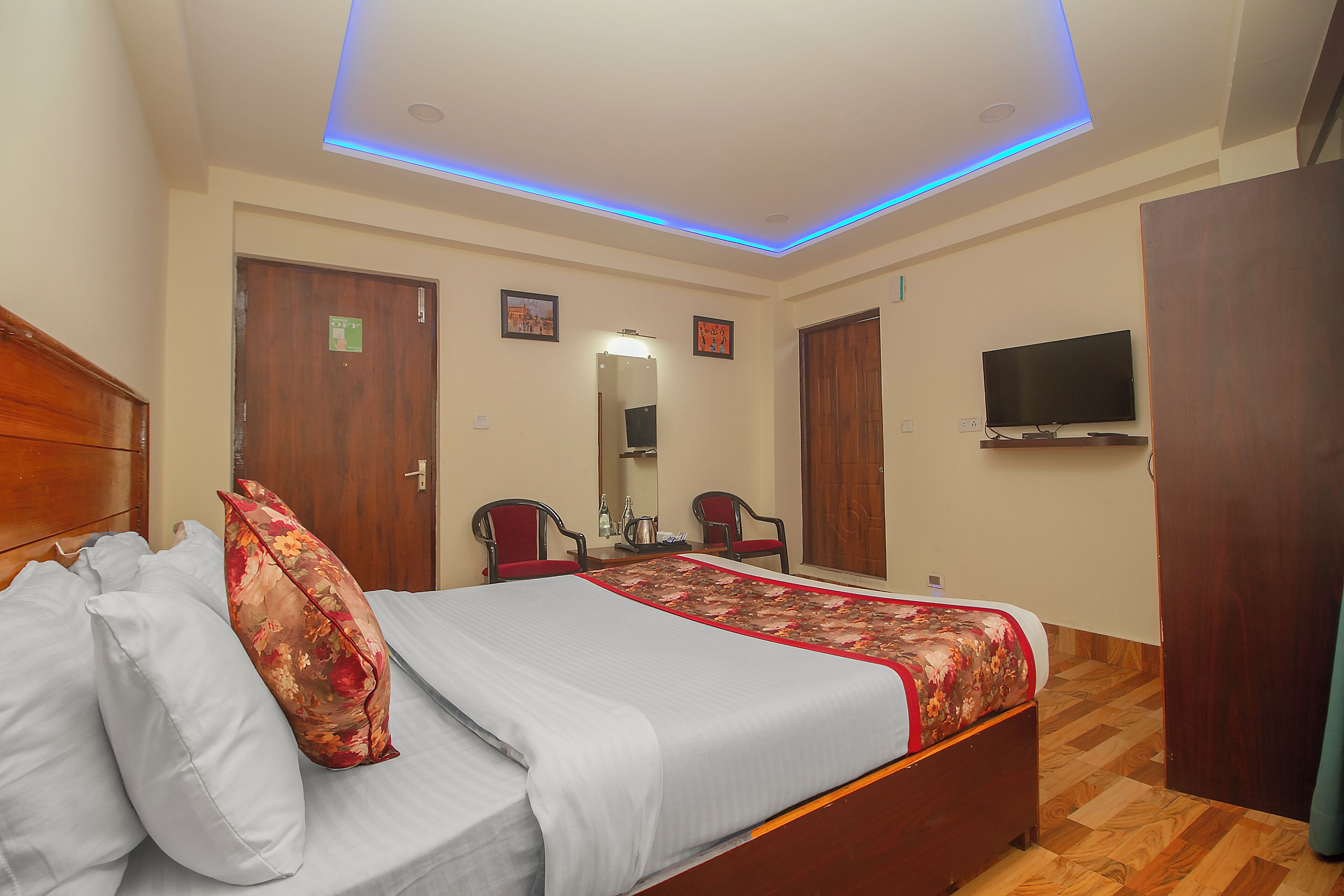 A hotel room with a bed, a TV, a desk with chairs, and a mirror.